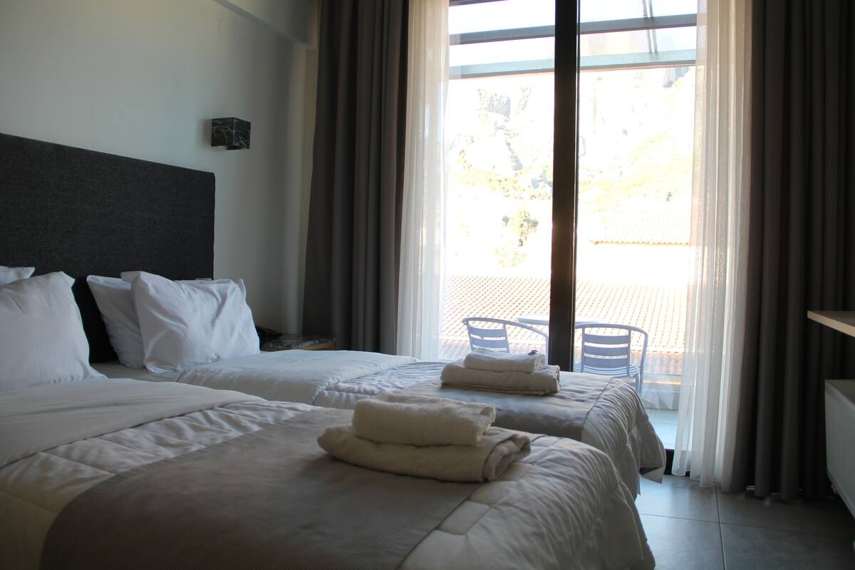 A hotel room with two beds, a large window with curtains, and a view of the outside.