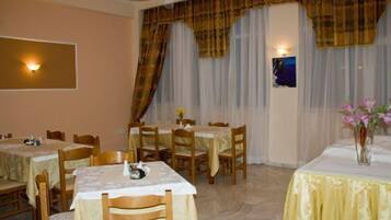 A dining area with multiple tables and chairs, a wall-mounted light fixture, and a window with curtains.