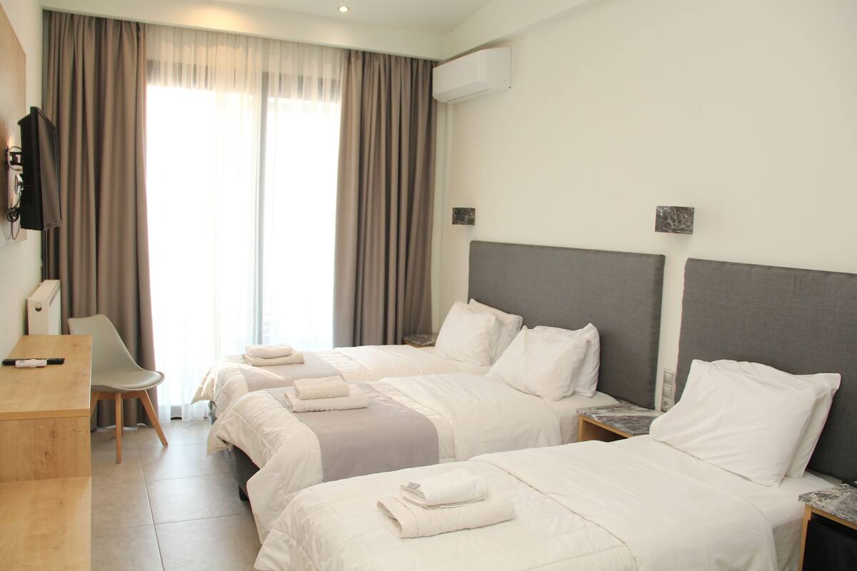 A hotel room with two beds, a desk, a chair, and a TV.