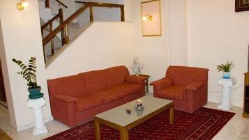 A living room with a staircase, two sofas, a coffee table, and a red patterned rug.