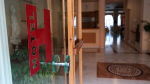 A hotel entrance with a glass door, a reception desk, and a patterned rug on the floor. - Alexiou Hotel (Kalabaka)