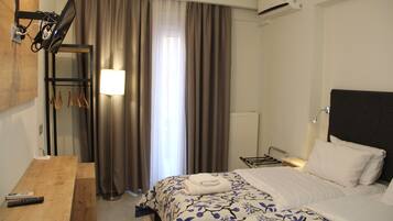 A hotel room with a bed, a desk, a lamp, a hanging coat rack, and a window with curtains.