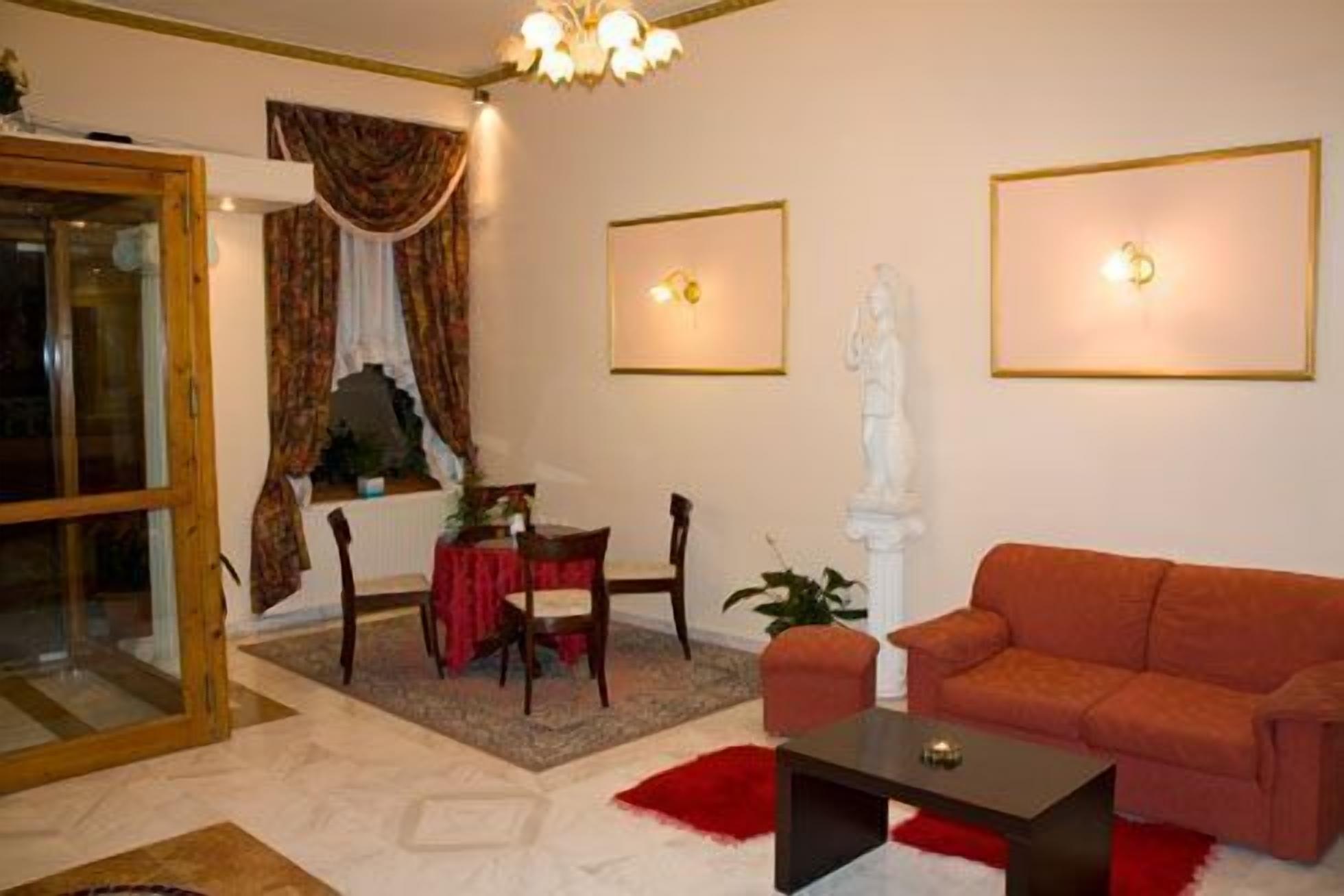 A living room with a sofa, a table, and a chair. There is a window with curtains, a statue, and framed pictures on the wall.