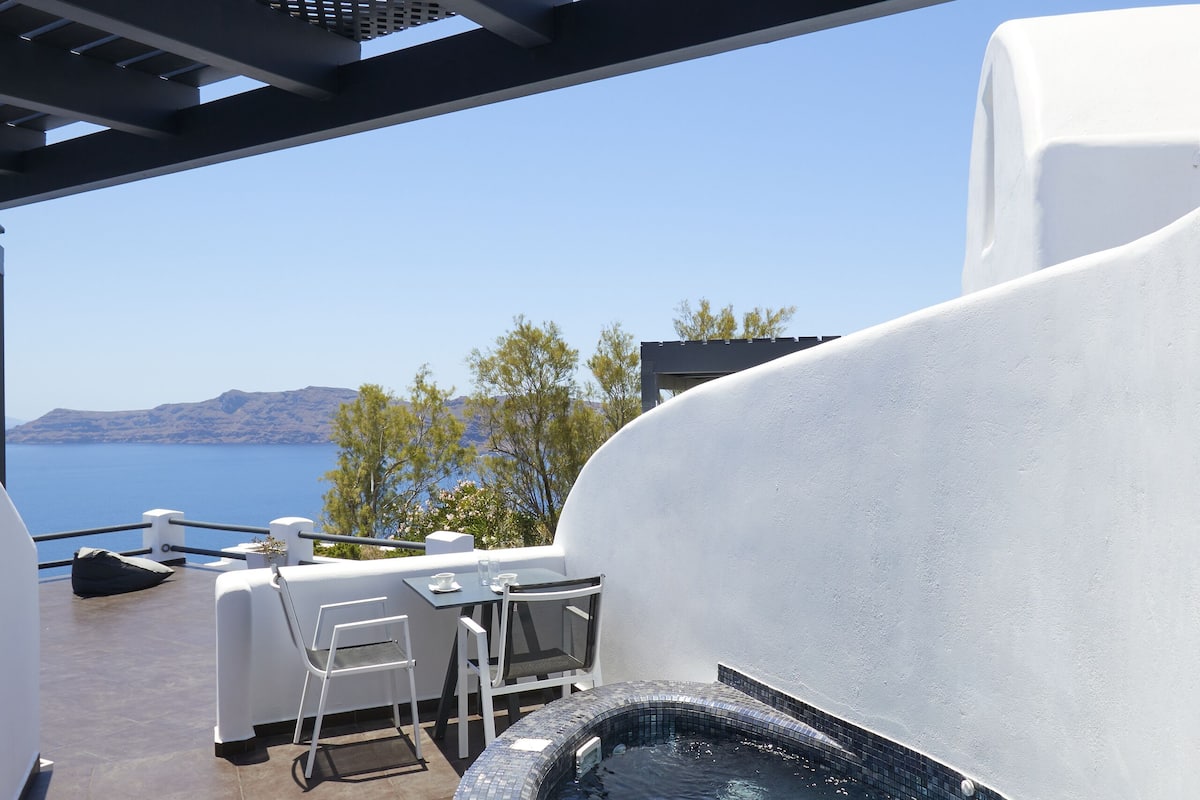 A modern outdoor hot tub area with a view of the sea, a covered seating area, and a lounge chair.