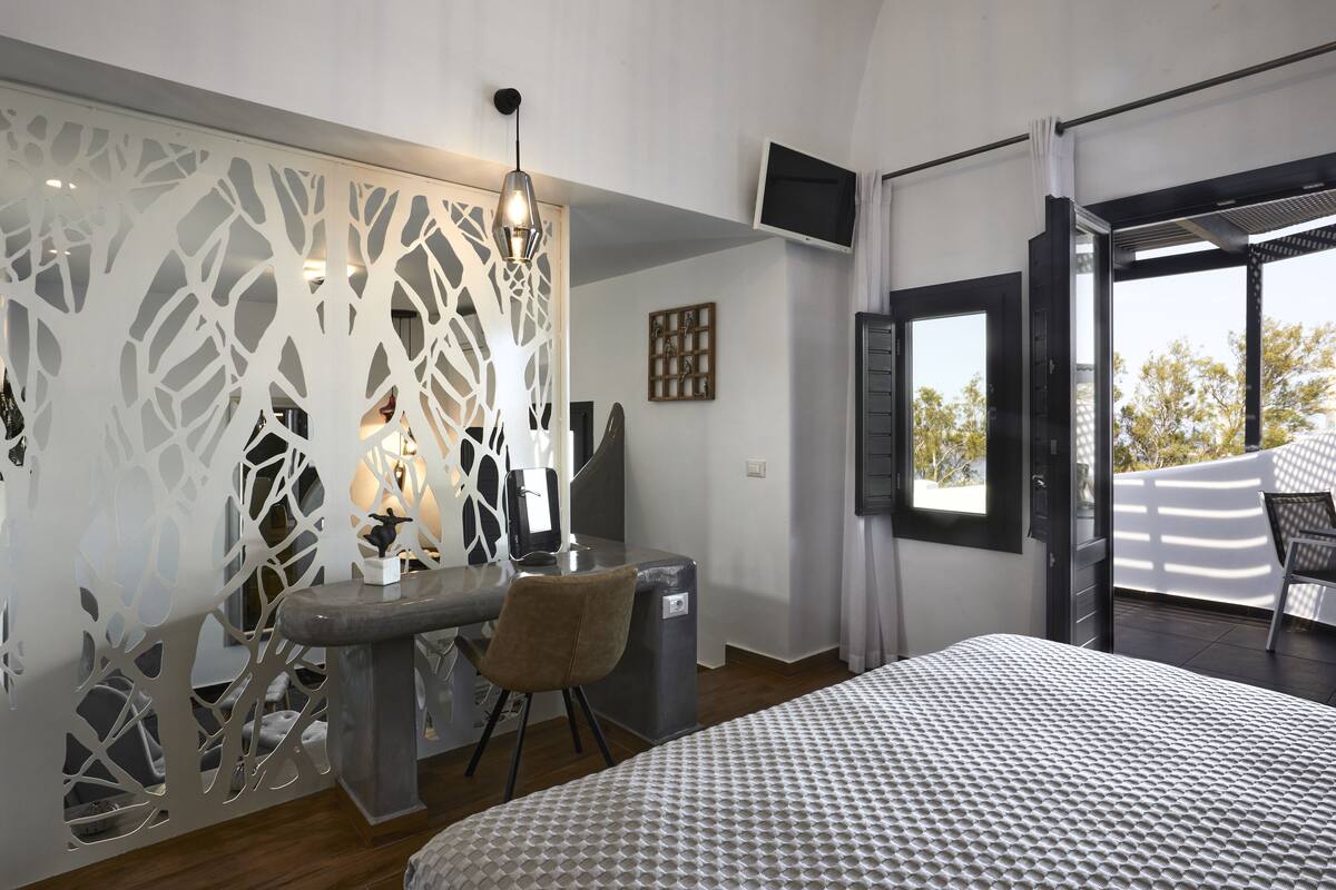 A bedroom with a bed, a desk with a chair, a TV, and a balcony.