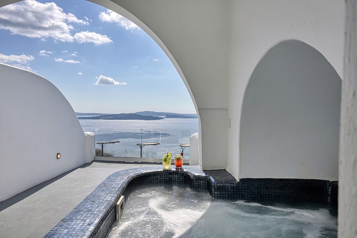 A hot tub with a view of the sea, a tiled floor, and a table with drinks.