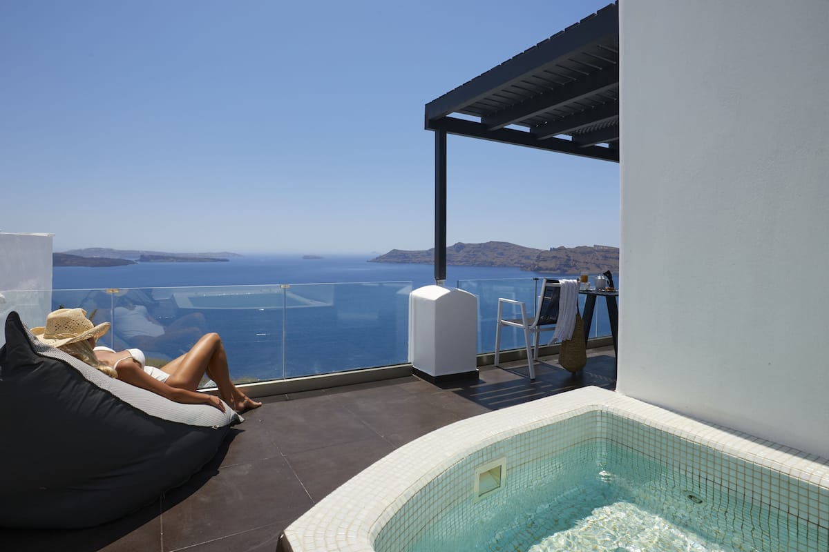 A balcony with a view of the sea, a hot tub, and a lounge area with a bean bag and a chair.
