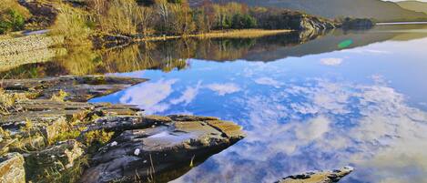 A calm lake with clear reflections, rocky shores, and distant mountains.