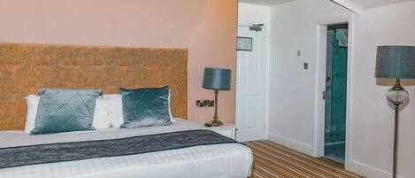 A hotel room with a bed, a nightstand, a lamp, and a door leading to another room.