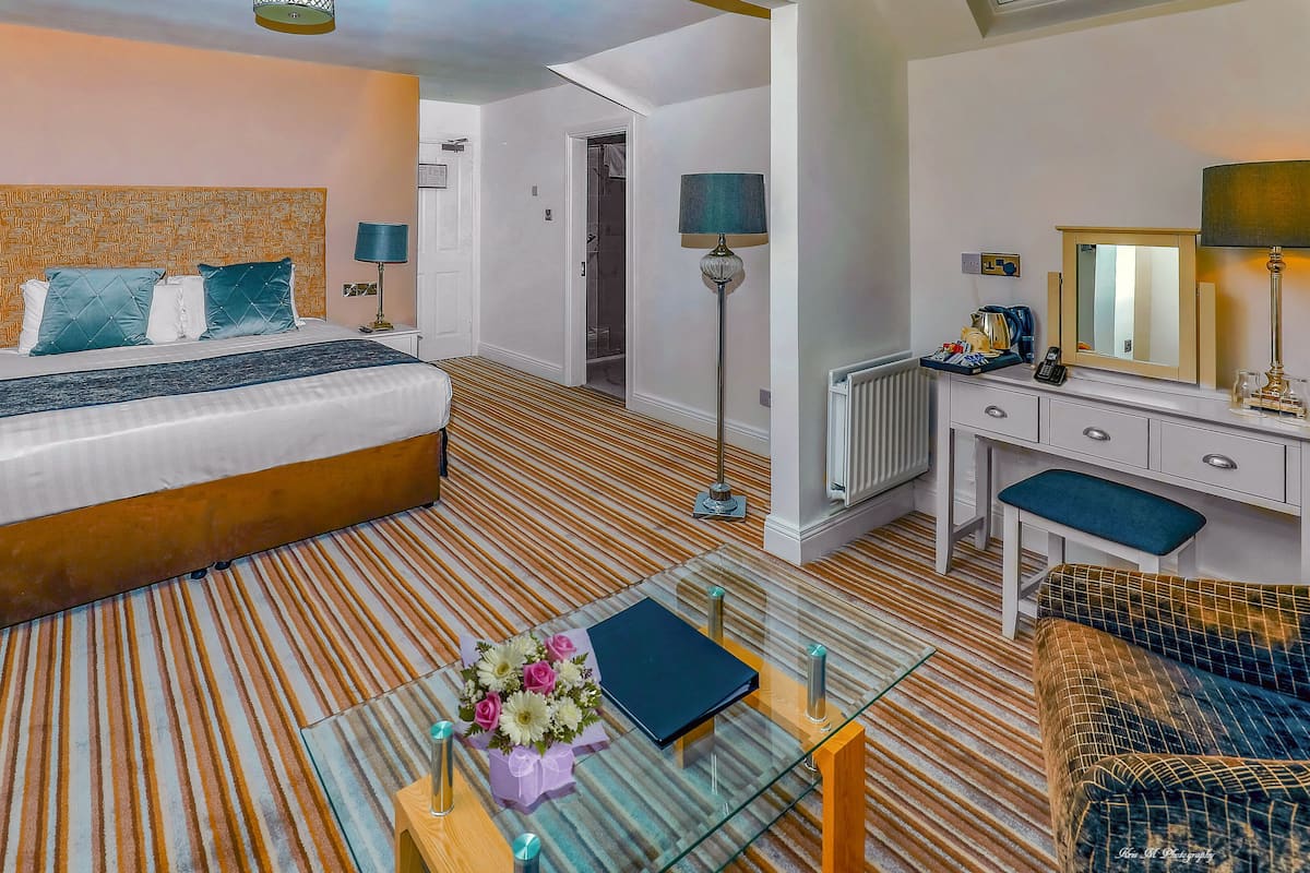 Une chambre d’hôtel avec un lit, une table de chevet, un bureau, une chaise et une table basse en verre ornée de fleurs et d’un livre.