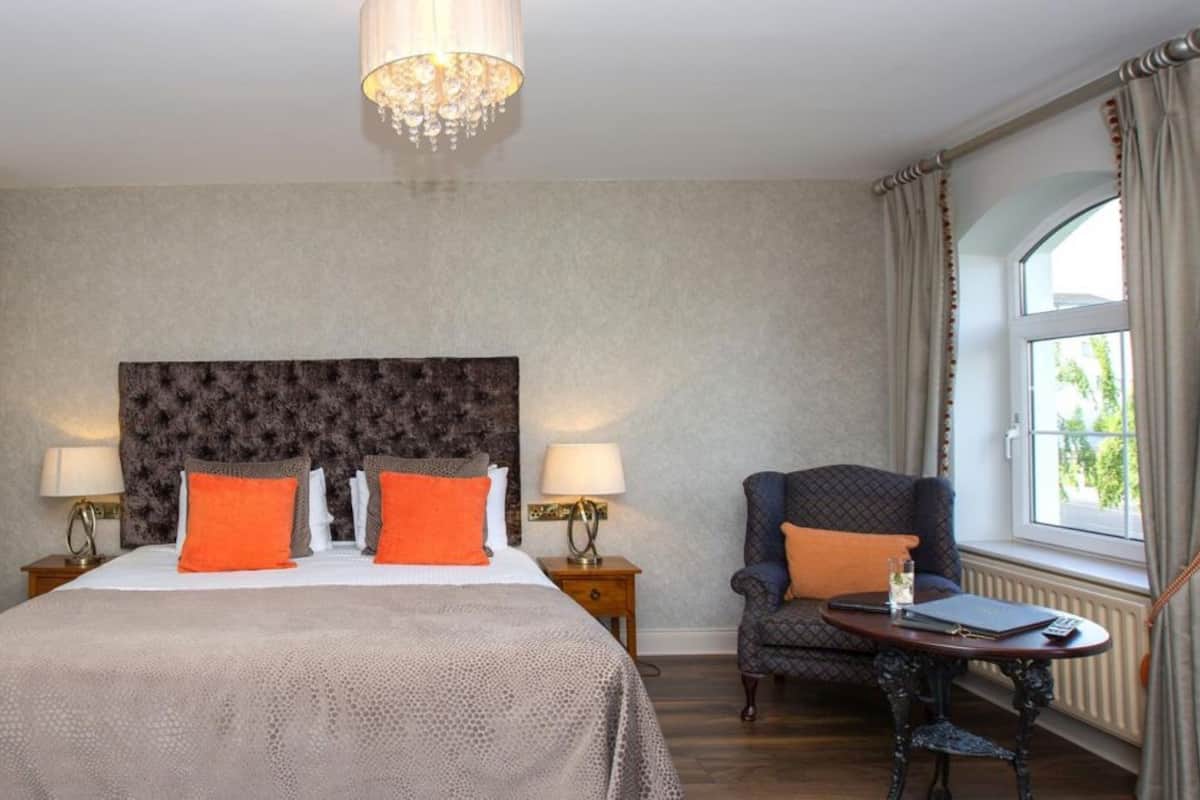 Une chambre d’hôtel avec un grand lit, une chaise, une table et une fenêtre avec des rideaux.