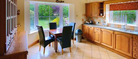 A kitchen with wooden cabinets, a dining table with chairs, a window with a view of greenery, and a hanging light fixture.