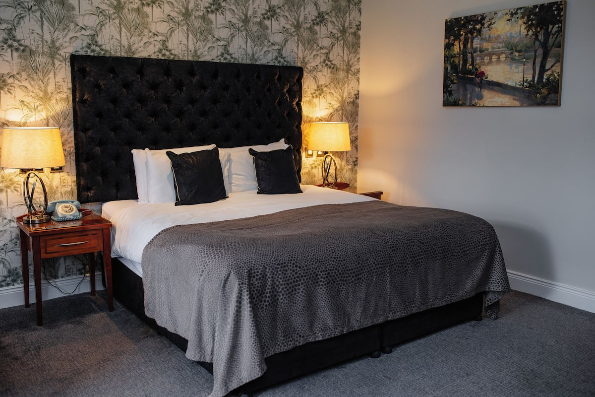 Une chambre à coucher avec une tête de lit capitonnée, un lit avec une literie blanche et noire, deux lampes de chevet et un tableau au mur.