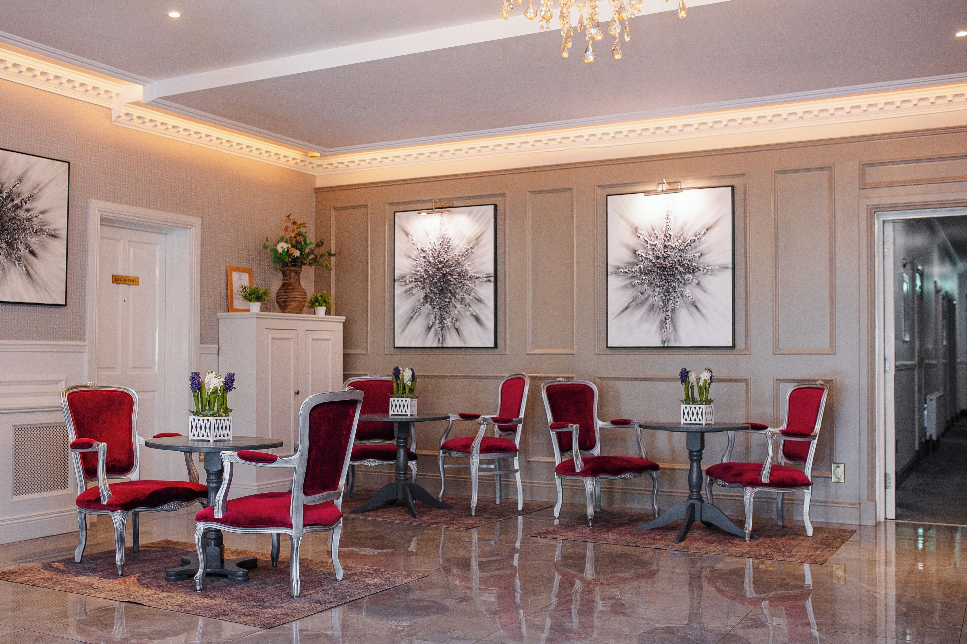 A hotel lobby with a chandelier, red upholstered chairs, a round table, and framed artwork on the walls.