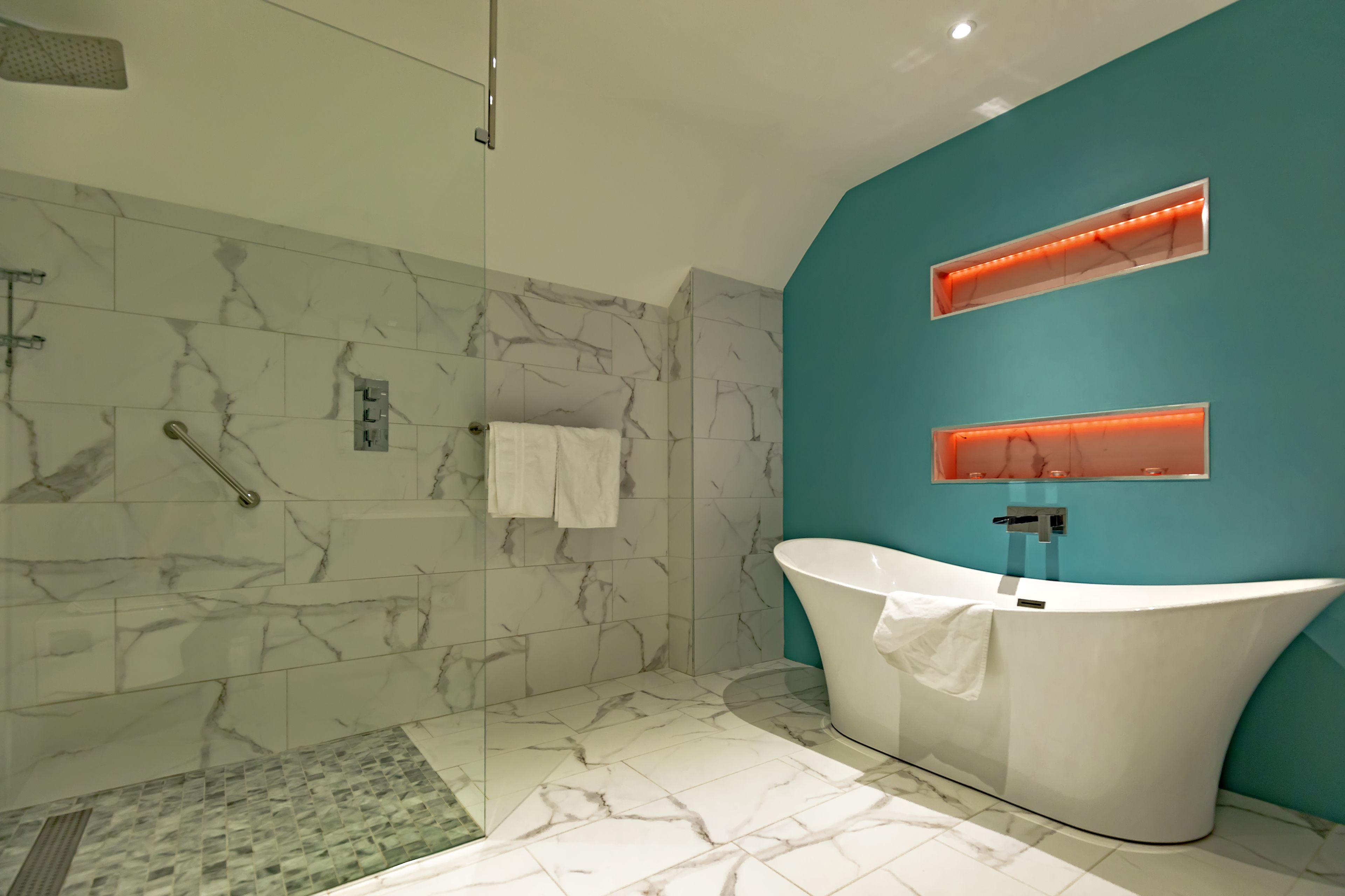 A modern bathroom with a freestanding bathtub, marble-tiled walls, and a glass-enclosed shower area.