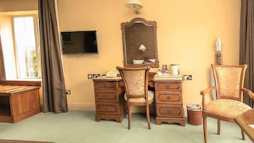 A hotel room with a desk, two chairs, a television, a mirror, and a window with curtains.