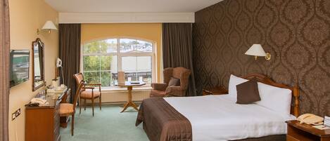 Ein Hotelzimmer mit einem großen Bett, zwei Nachttischen, einem Schreibtisch mit Stuhl, einem Fernseher und einem Fenster mit Vorhängen.
