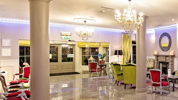 A hotel lobby with a polished marble floor, red and green upholstered chairs, a chandelier, and a fireplace. - Brook Lodge Boutique Hotel (Killarney)