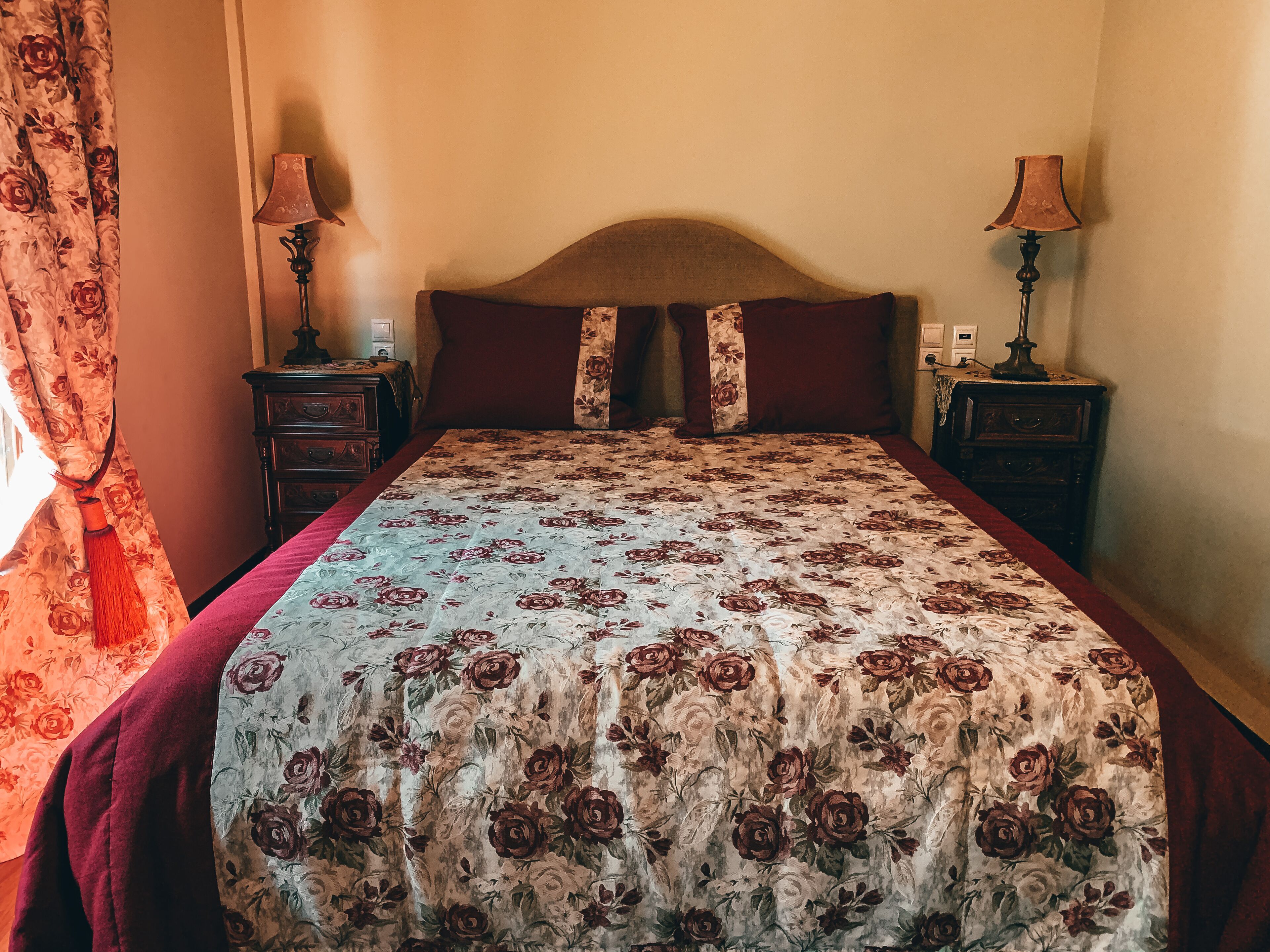 A bedroom with a bed, two nightstands, a lamp on each, and a floral bedspread.