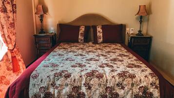 Een slaapkamer met een bed, twee nachtkastjes en een lamp op elk, en een bloemenbedekking.