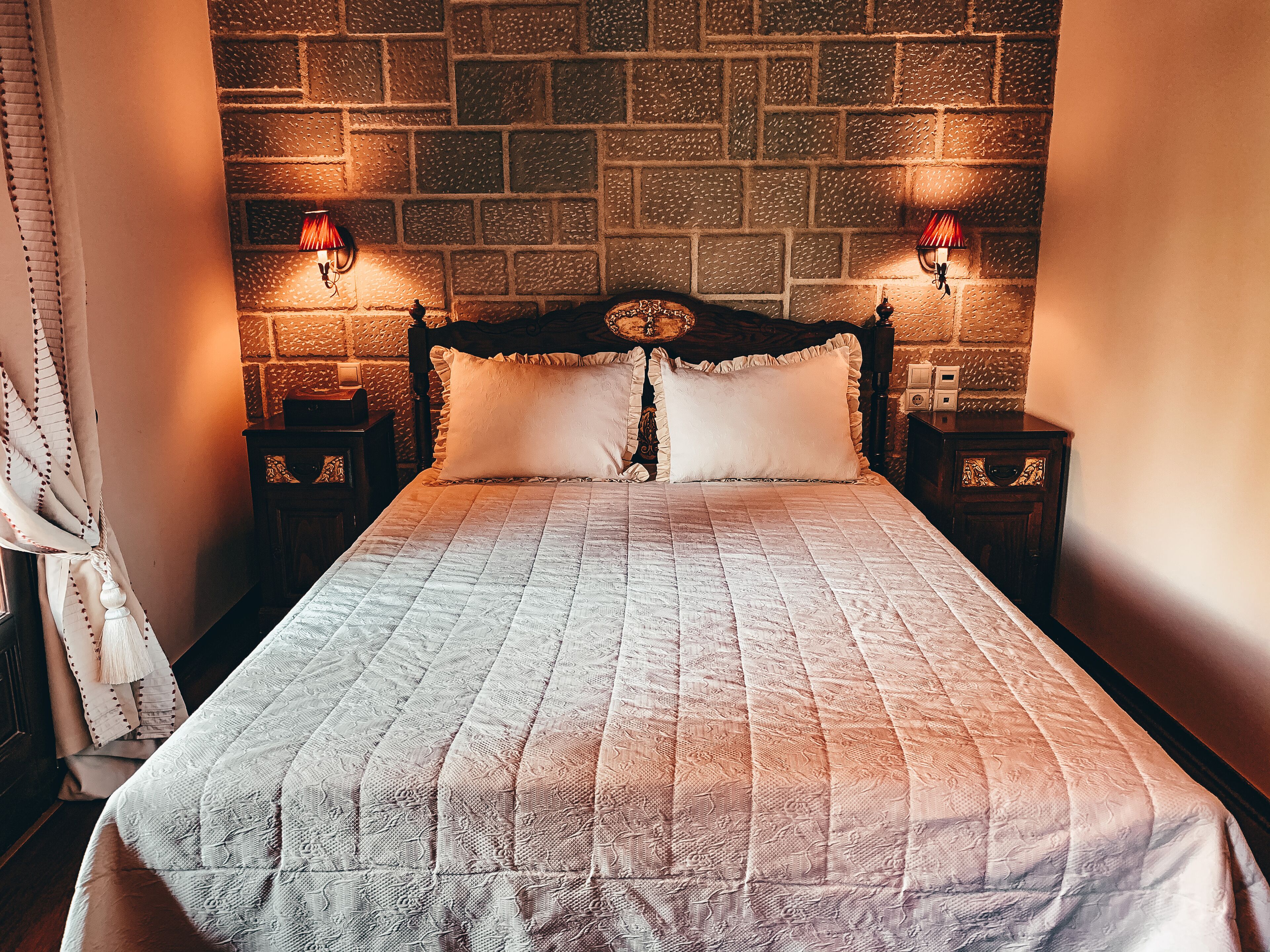 A bed with a quilt, two bedside tables with lamps, a headboard, and a brick-patterned wall.