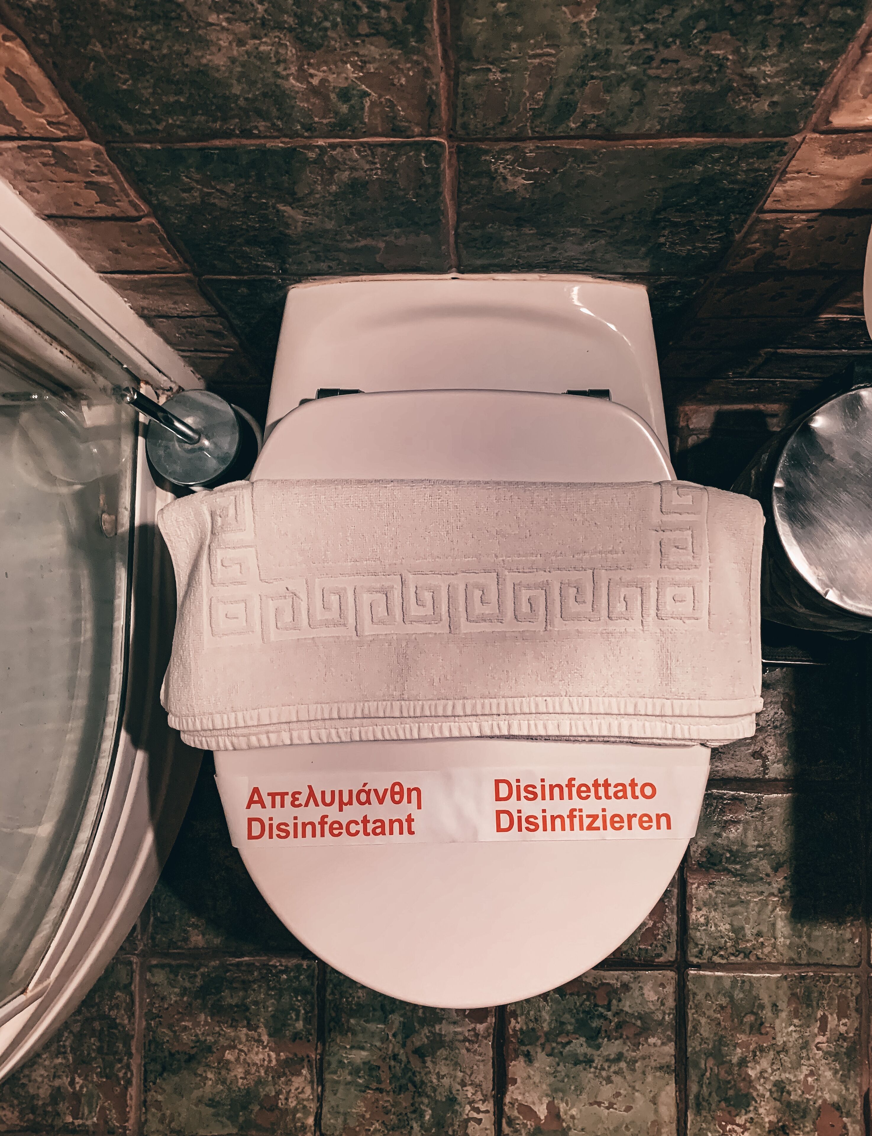 En toalett med ett vitt lock och en handduk ovanpå. Det finns etiketter på två språk som anger ”desinfektionsmedel”.