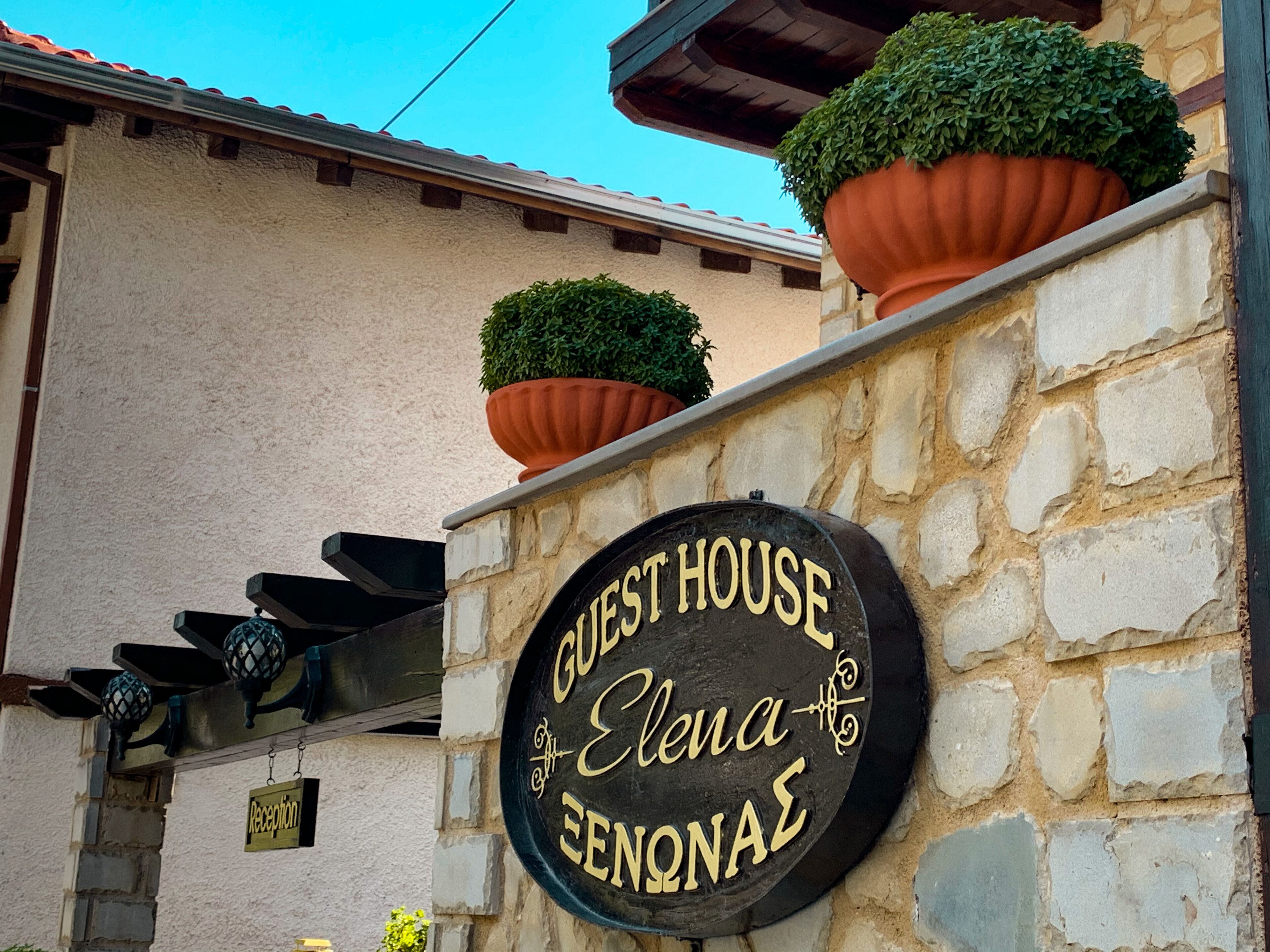 A stone wall with a sign reading "GUEST HOUSE Elena ENONAES".