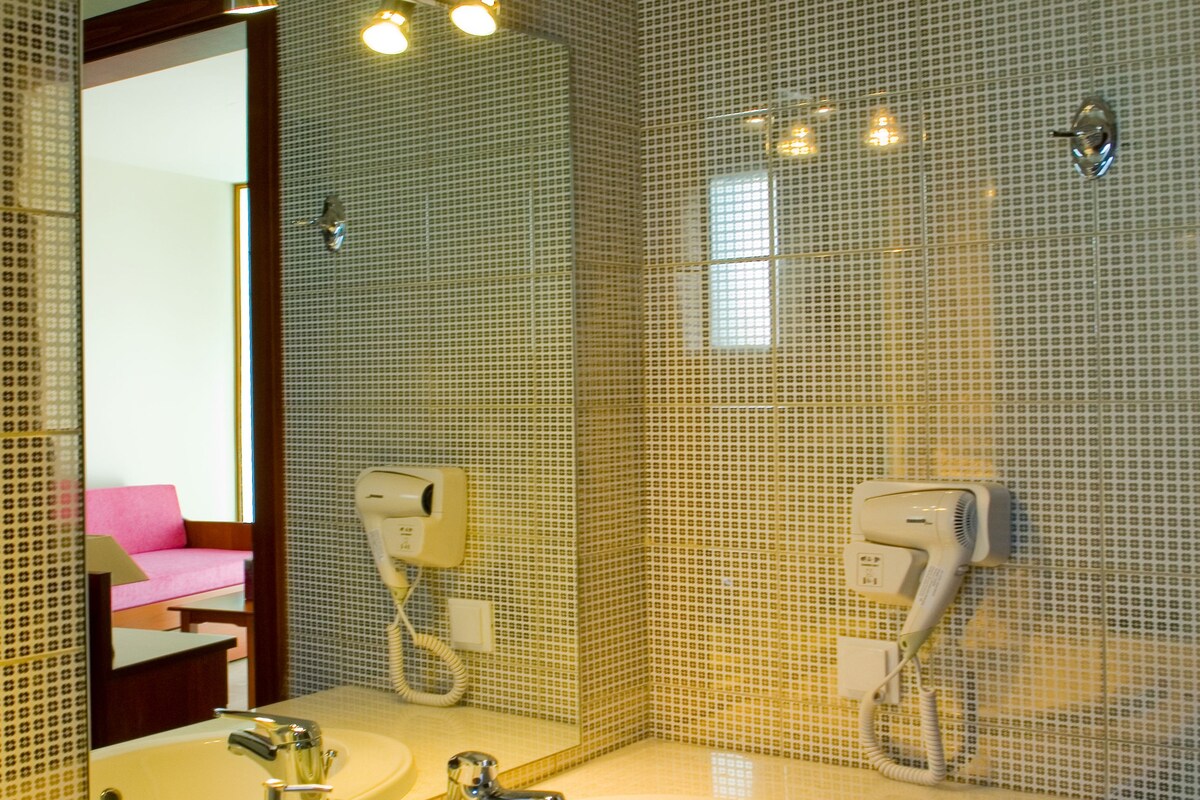 A bathroom with two sinks, a large mirror, and hair dryers mounted on the wall.