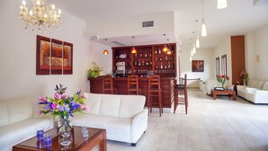 A spacious living area with a white sofa, a coffee table, and a bar area with shelves of bottles. - Syia Hotel (Kantanos-Selino)