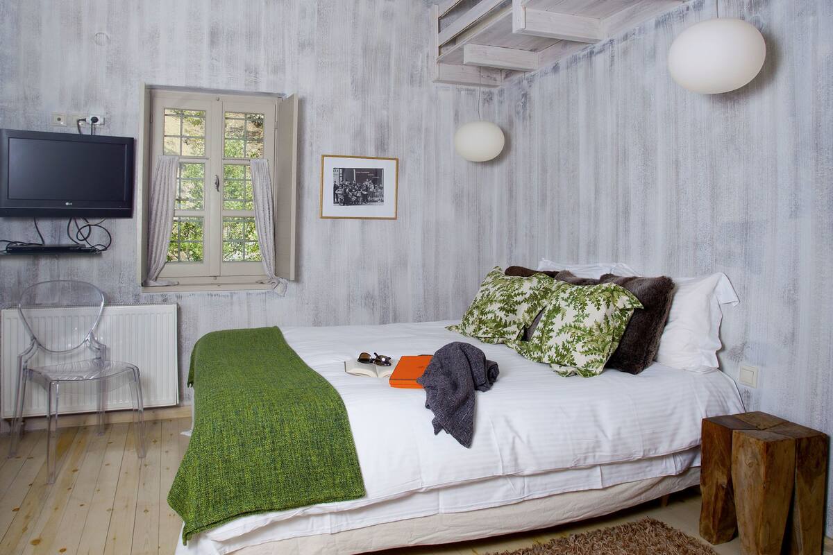 Een slaapkamer met een bed, een televisie, een raam en een houten plafond.