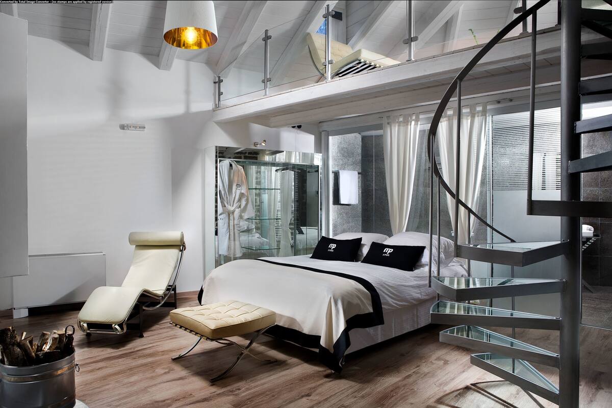 Een moderne slaapkamer met een bed, een fauteuil, een douche met glazen wanden en een spiltrap.