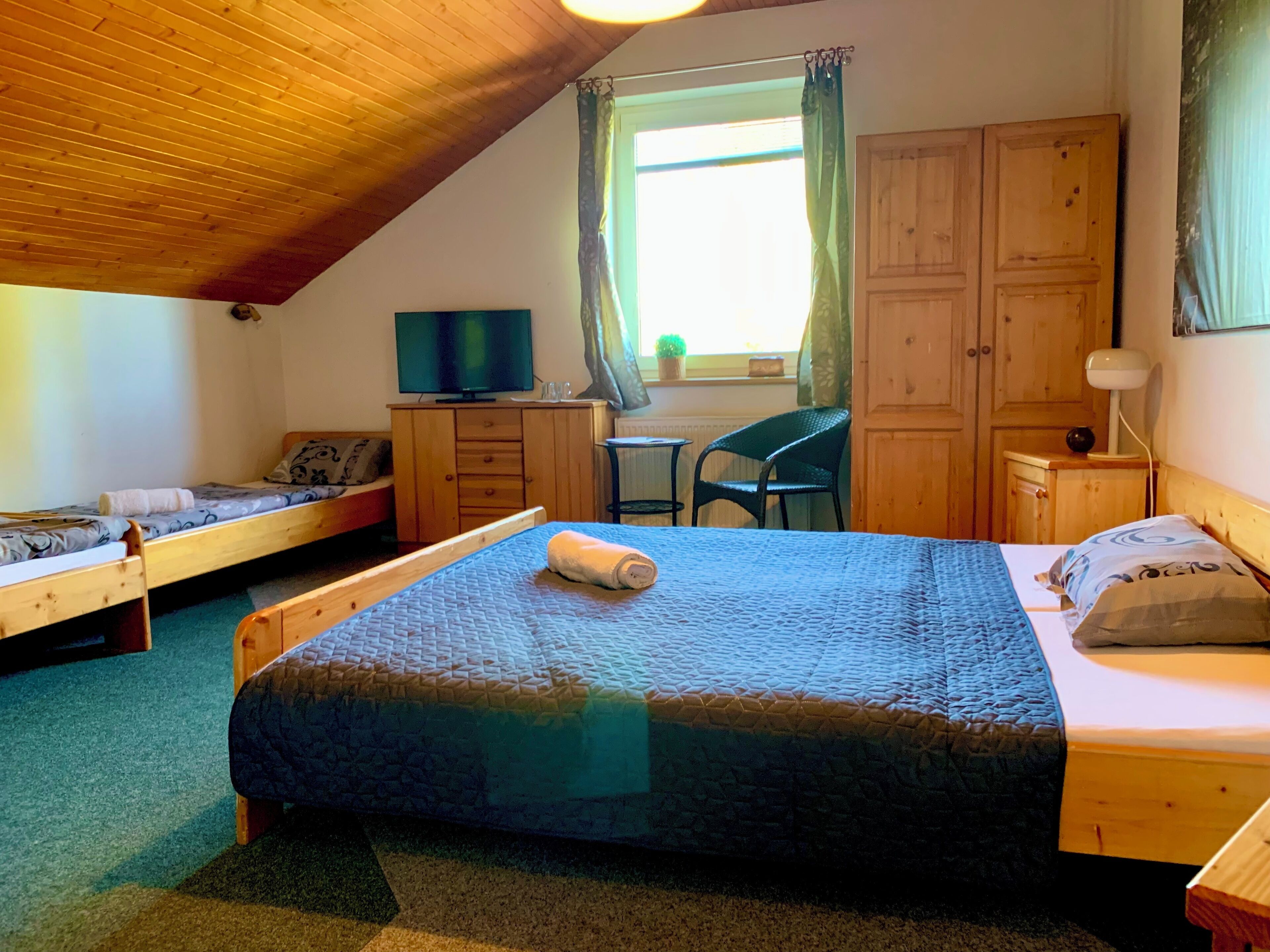 Ein gemütliches Zimmer mit einem großen Bett, einem Einzelbett, einem Schreibtisch, einem Stuhl, einem Fernseher und Holzschränken.