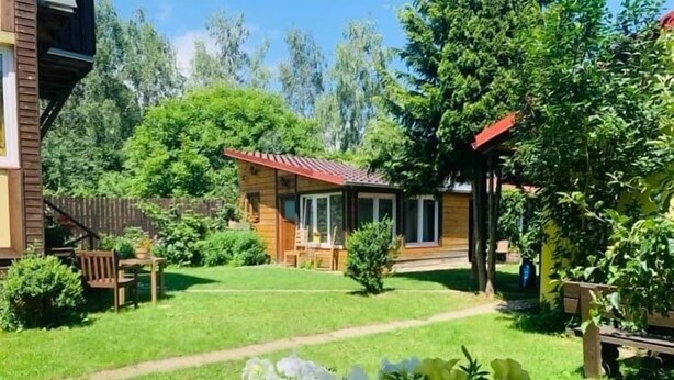A wooden house with a red roof, surrounded by a well-maintained lawn and various plants. - Pension Aqualand (Poprad)