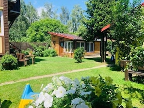 Une maison en bois avec un toit rouge, entourée d’une pelouse bien entretenue et de diverses plantes.