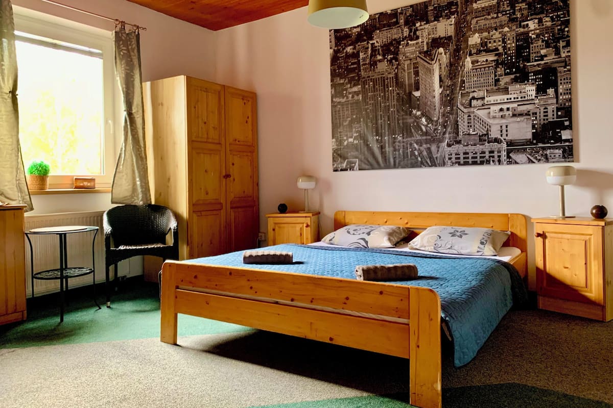 A bedroom with a wooden bed, a cityscape poster, a desk with a chair, and a window with curtains.