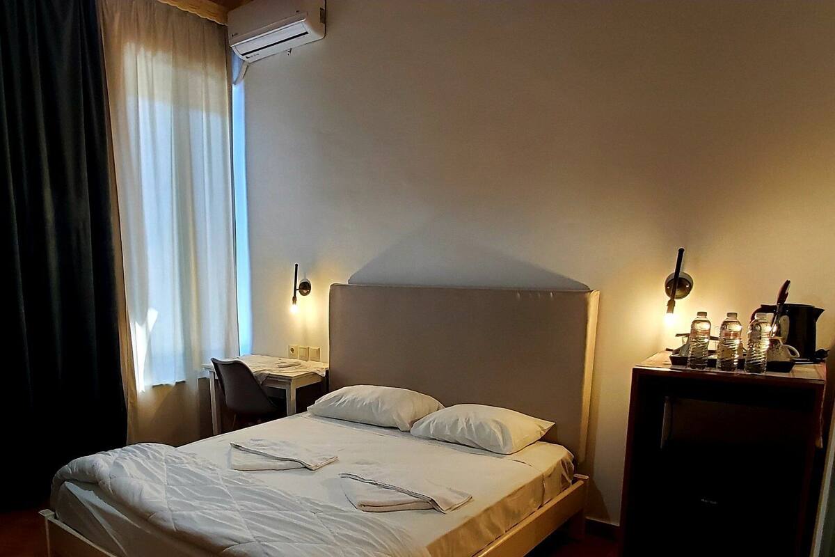 A neatly made bed with pillows, a bedside table with a lamp, and a small desk with a water bottle.