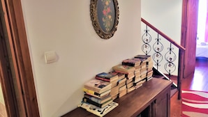 A wooden console table with a stack of books, a framed picture on the wall, and a staircase with a metal railing. - Diporto (Chania)