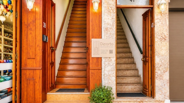 A hotel entrance with a wooden staircase, a sign for rooms for rent, and a potted plant. - Diporto (Chania)