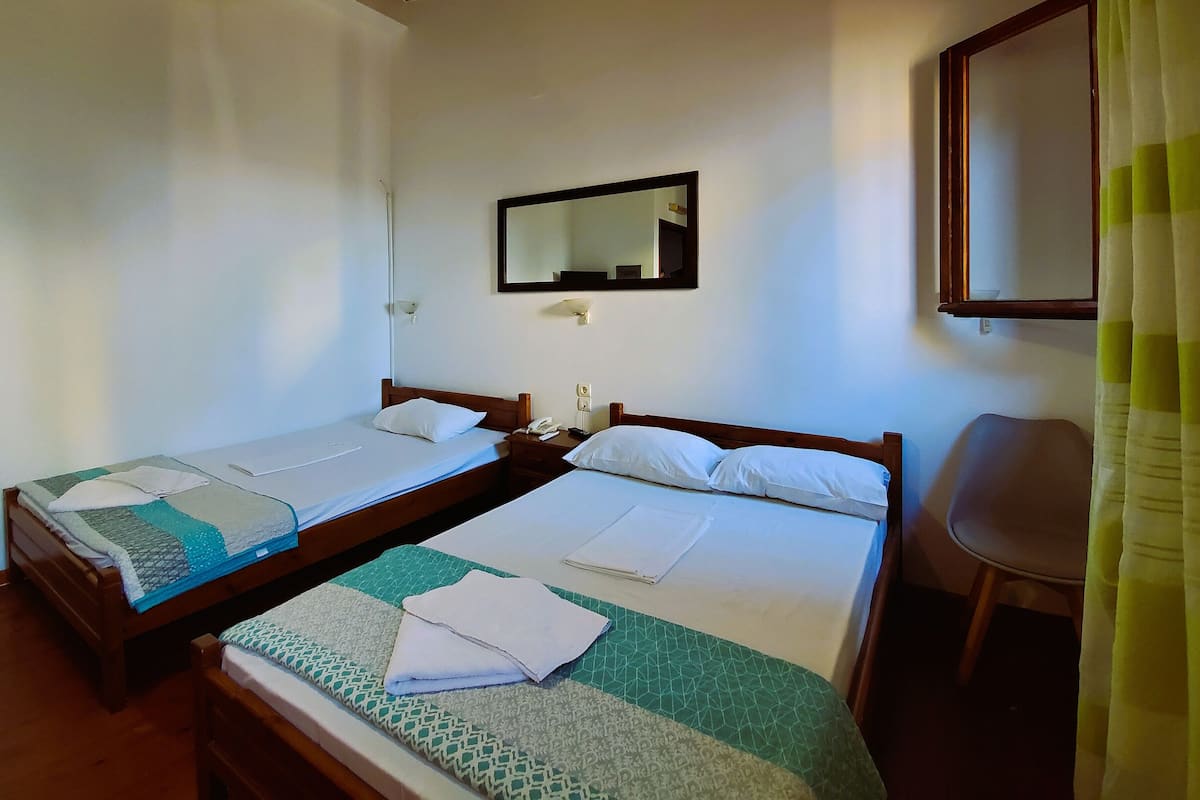 A hotel room with two single beds, a bedside table with a phone, a mirror, and a chair.