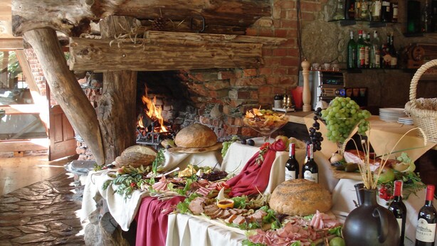 A rustic dining table with a variety of food and drinks, a fireplace in the background, and a brick wall. - Rezydencja Bialy Jar (Karpacz)
