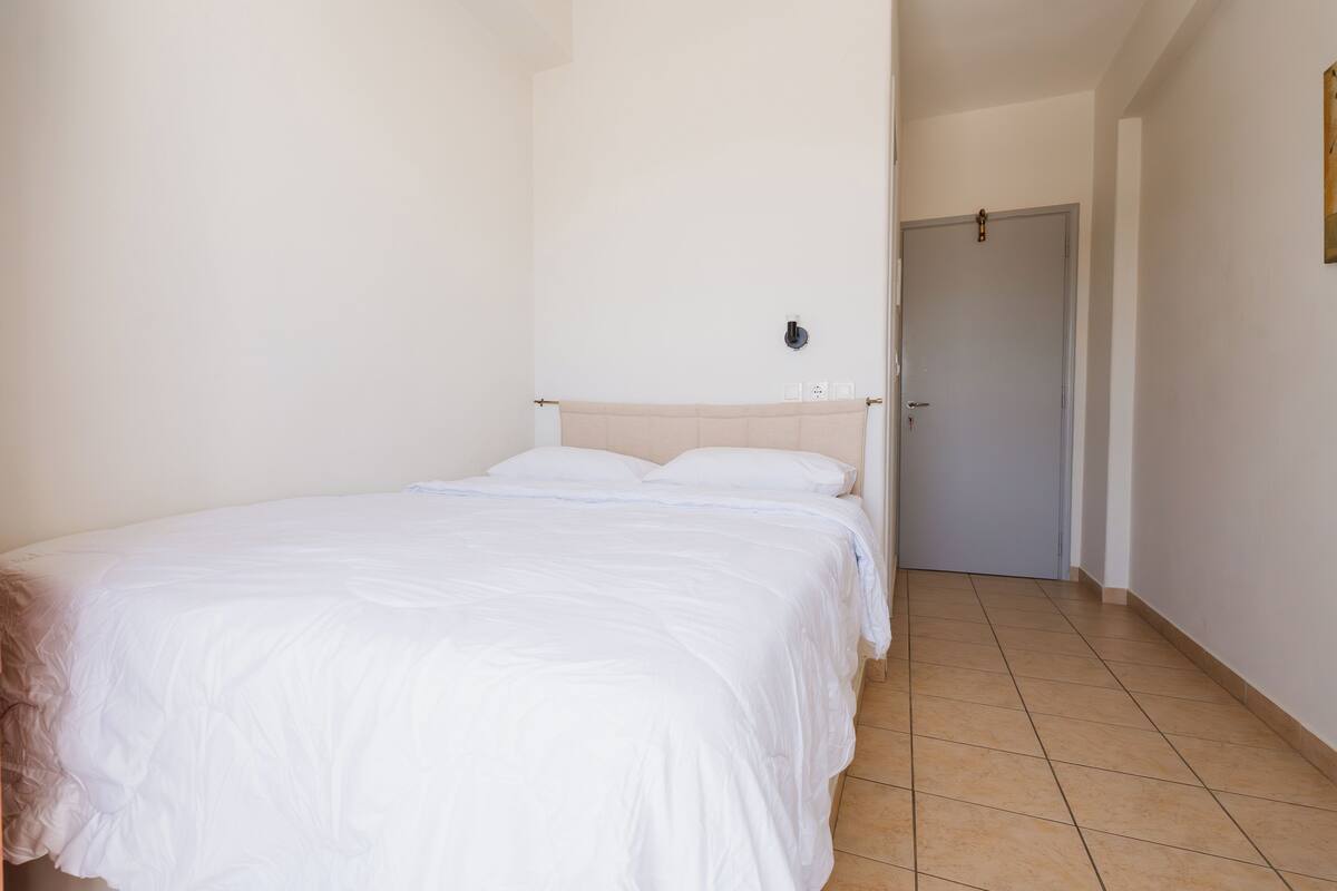 A bedroom with a bed, a door, and a light switch on the wall.