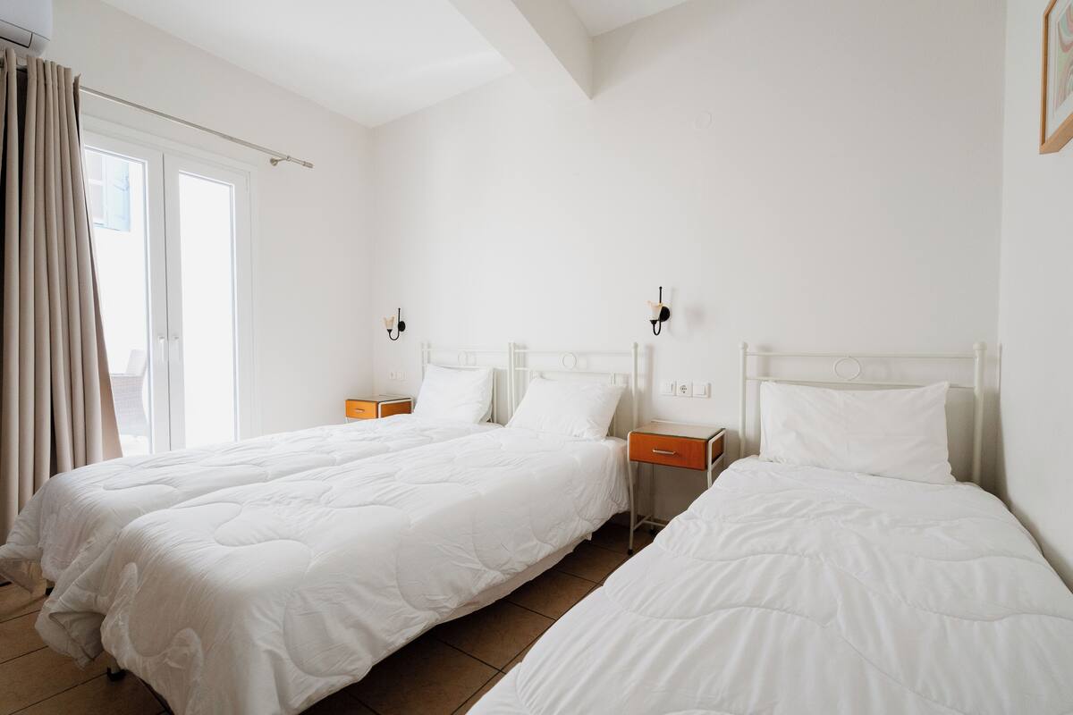A hotel room with two beds, a window with curtains, and a nightstand with a lamp.
