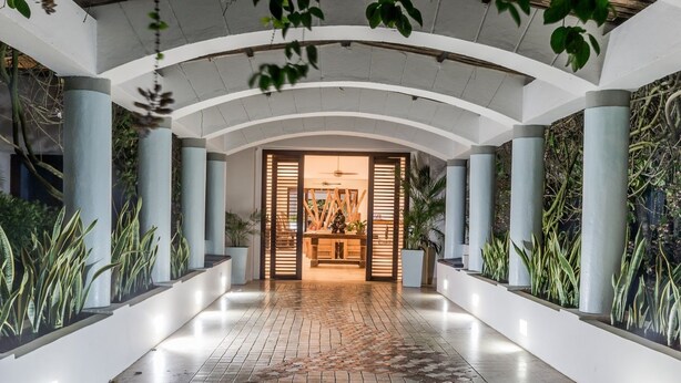 Een moderne hotelgang met een tegelvloer van baksteen, witte muren en zuilen.