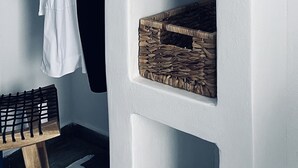 A room with a white wall, a wooden bench, and a clothing rack with a white and black garment.