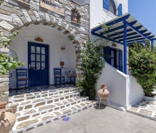 A stone building with a blue door and windows, a stone staircase, and a covered outdoor seating area.