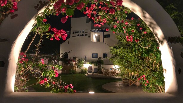 A white building with a sign reading "ANGIE'S STUDIO" under a large archway adorned with pink flowers.
