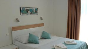 A single bed with a wooden headboard, two pillows, a teal bedspread, and a small bedside table.