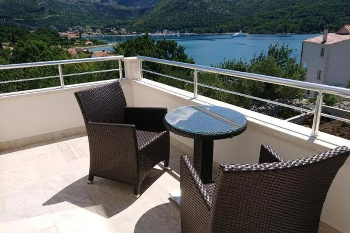Un balcón con mobiliario de mimbre y una mesa de vidrio, con vista a un lago y montañas.