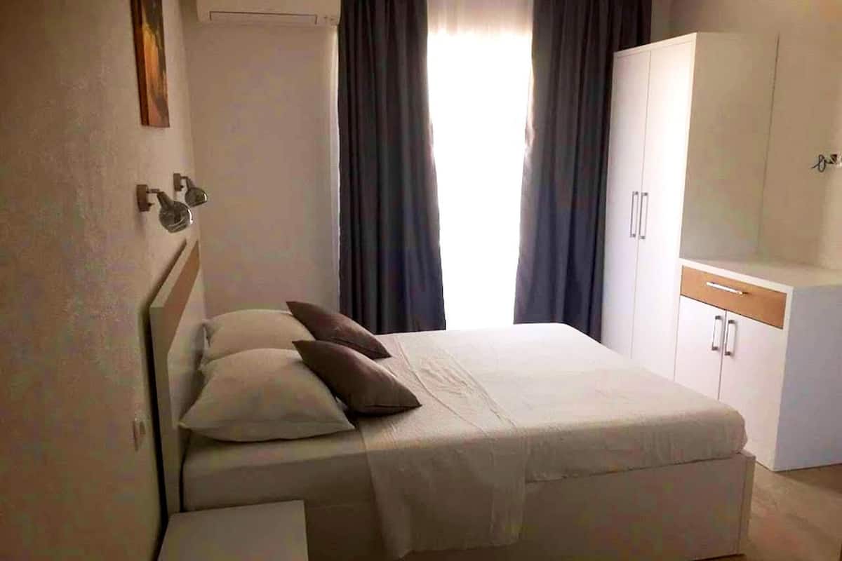 Un dormitorio con cama, mesita de noche, armario y ventana con cortinas.