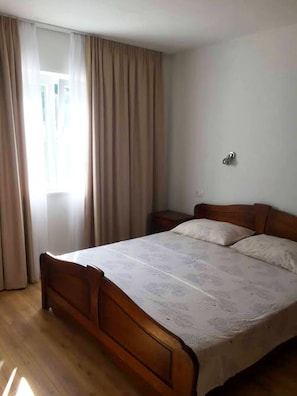 Quarto com cama de madeira, mesa de cabeceira e janela com cortinas.